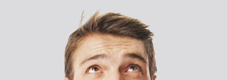 Man with short brown hair looking up towards his hairline against a light grey background