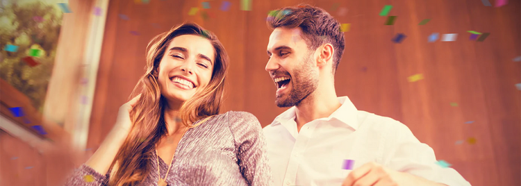 Smiling woman and a laughing man in a white shirt standing close together as confetti falls around them