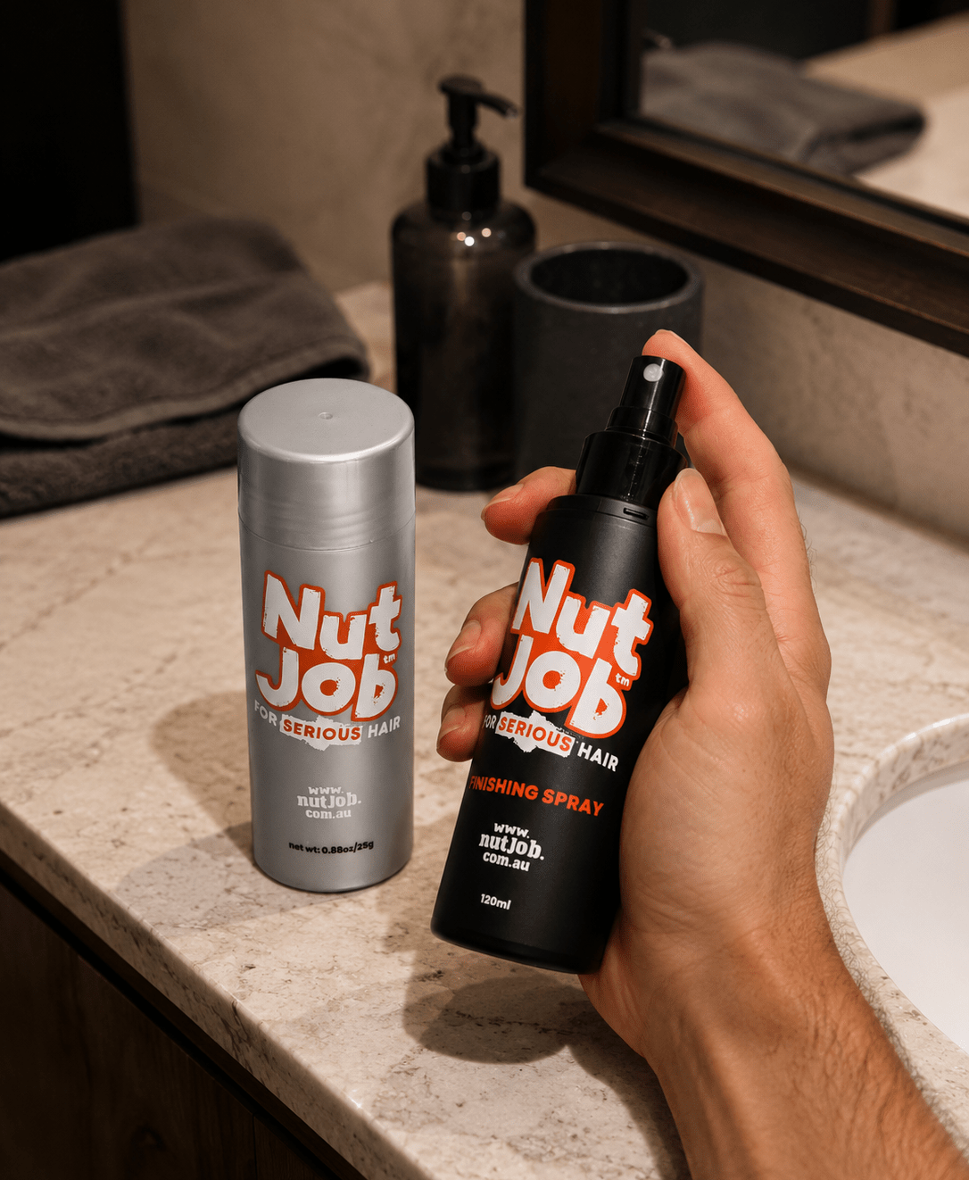 Hand holding Nut Job Finishing Spray beside a Nut Job Hair Building Fibres bottle on a bathroom vanity