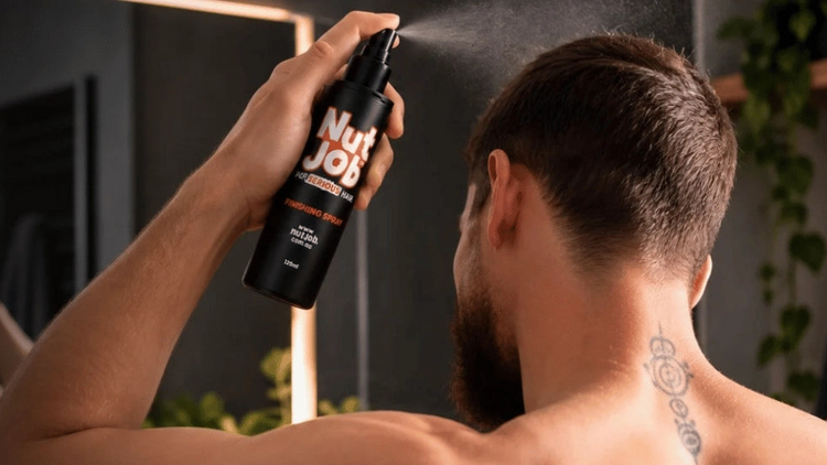 Man seen from behind spraying Nut Job Finishing Spray onto his hair at a bathroom mirror